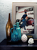 Decorative objects, vase and ceramic jugs in front of a retro advertising poster