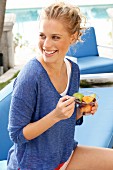 A blonde woman wearing a blue long-sleeved top and eating a fruit salad