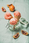 Refreshing summer blood orange ice cream or sorbet scoops in sweet waffle cones in glass jar