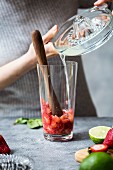 Frau giesst Limettensaft für Erdbeer-Margarita ins Glas