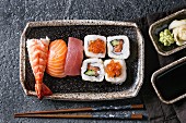 Sushi Set nigiri and sushi rolls in dark ceramic plate with soy sauce and chopsticks over black stone texture background