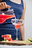 A woman pouring watermelon margarita from a jug into a rimmed margarita glass