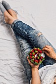 A woman with jeans sitting and holding a plate of fresh strawberries