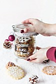 Hands holding a glass jar with decorated Christmas cookies