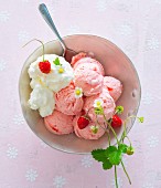 A bowl of strawberry ice cream, whipped cream and wild strawberries