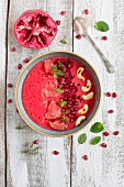 A red smoothie bowl with grapefruit, raspberries, pomegranate seeds and cashews