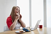 Young woman with laptop eating sandwich
