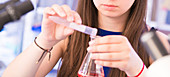 Chemistry student pouring liquid into beaker