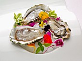 A plate of three oysters on half shell garnished with edible flowers