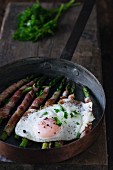 Bacon-wrapped green asparagus in a pan with a fried egg