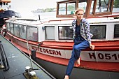 Blonde Frau in gemustertem Blazer und Jeans-Overall auf einem Boot