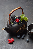 A teapot with fresh berries and tea leaves
