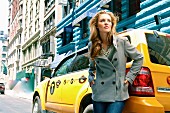 A blonde woman wearing a grey wool jacket and jeans in front of a yellow cab