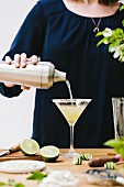 Frau giesst Martini aus Cocktailshaker in ein Glas