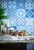 Mousse au Chocolate in Gläsern auf Holztisch vor blau-weiss gefliesster Wand