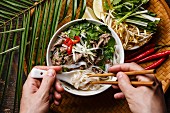 Pho Bo Soup with beef and chopsticks in male hands