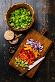 Geschnittenes frisches Gemüse auf Holzbrett daneben Blattsalat in Olivenholzschüssel
