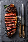 Sliced medium rare grilled Striploin steak with knife and fork on slate board