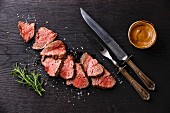 Sliced medium rare Roast beef with table knife and fork for meat on dark background