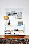 Blue console table with piles of books under the framed photo