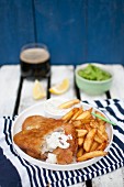 Fish and chips, served with mashed green peas, pieces of lemon tartare sauce and dark beer