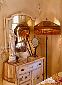 Old standard lamp with fringed shade next to shabby-chic chest of drawers