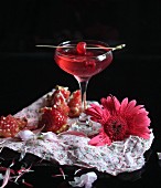 A cocktail with pomegranate, raspberries, and a cocktail cherry
