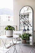 Bistro table and chairs in front of large wall-mounted mirror on balcony