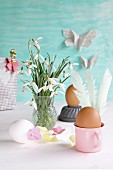 Eggs decorated for Easter with feathers and paper flowers next to vase of snowdrops