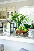 Green apples in fruit bowl, candle lantern and vase of white lilies on kitchen worksurface