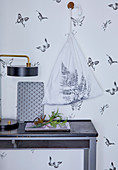 Cloth bag printed with fern leaf hung on wall with butterfly-patterned wallpaper