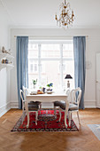Classic dining table with medallion chairs on Oriental rug in front of window