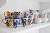 Blue-patterned mugs with gilt handles on shelf