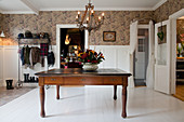 Old wooden table in large foyer with white wainscoting and brown wallpaper
