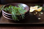 Fresh dill fronds in a wood bowl and lemon wedges