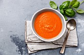 Tomato soup Gazpacho in bowl and green basil on grey concrete background
