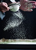 A cooks hands sprinking icing sugar on to a baking tray