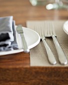 A place setting with cutlery and napkins on a wooden table (close up)