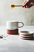 Honig fliesst von Honiglöffel in Keramikbecher mit Tea Latte