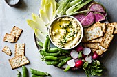Frühlingsgemüse und Cracker mit Hummus-Dip auf Teller (Aufsicht)