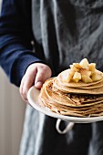 A boy holding a plate with a stack of pancakes and apple sauce