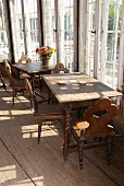 Alte Holztische und Stühle mit gedrechselten Stuhlbeinen auf rustikalem Bretterboden vor Fenster
