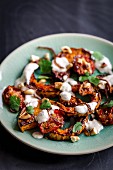 Slices of roasted butternut squash and tomatoes topped with ginger and garlic, yoghurt dressing and crispy shallots, coriander leaves and toasted cashews