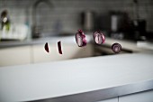 A sliced red onion floating in front of a kitchen scene over a white kitchen worktop