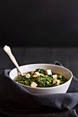 A white bowl filled with vegetarian wholegrain spelt miso soup with tofu, spinach and kale on a black wooden background