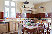 Wooden table and chairs in country-house kitchen with red tiled splashback