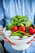 A man holding a colander of fresh ingredients for making Mexican sauce