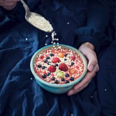 A woman sprinkling quinoa pops over a vegan smoothie bowl with a spoon