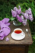 A cup of tea and a lilac blossom bouquet on a table outdoors