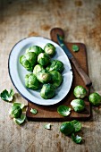 Brussels sprouts on a serving platter with a wooden chopping board and a knife